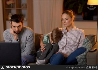 family, leisure and people concept - gloomy father, mother with sleeping little son watching something boring on tv at home at night. family watching something boring on tv at night