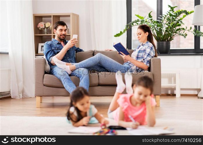 family, leisure and people concept - happy daughters with crayons drawing in sketchbooks, mother and father with tablet pc computer sitting on sofa at home. happy family spending free time at home