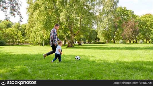 family, leisure and people concept - happy father and little son with ball playing soccer at summer park. happy father and son playing soccer at summer park