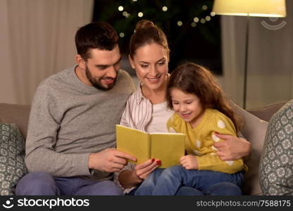 family, leisure and people concept - happy father, mother and little daughter reading book at home at night. happy family reading book at home at night