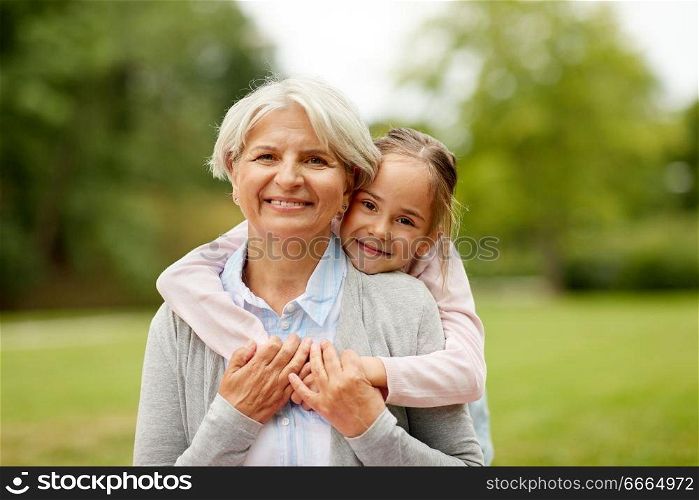 family, leisure and people concept - happy granddaughter hugging her grandmother at summer park. granddaughter hugging grandmother at summer park