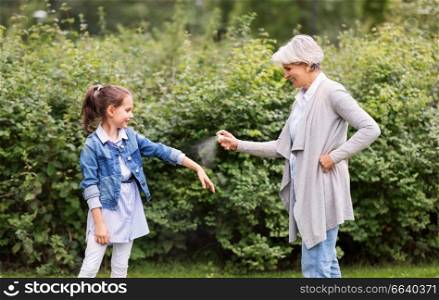 family, leisure and people concept - happy grandmother and granddaughter applying insect repellent spray at summer park. grandma and granddaughter with insect repellent