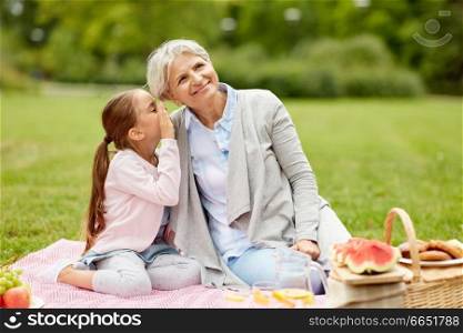 family, leisure and people concept - happy grandmother and granddaughter having picnic at summer park and sharing secrets. grandmother and granddaughter at picnic in park