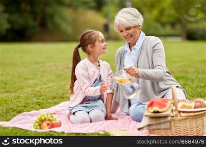 family, leisure and people concept - happy grandmother and granddaughter having picnic and drinking fruit water at summer park. grandmother and granddaughter at picnic in park