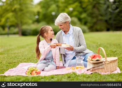 family, leisure and people concept - happy grandmother and granddaughter having picnic at summer park. grandmother and granddaughter at picnic in park