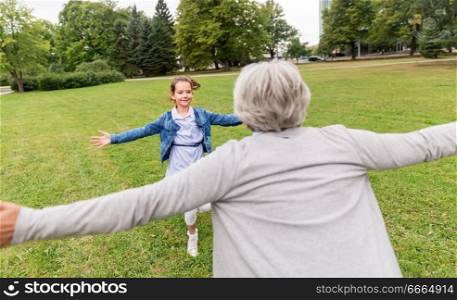 family, leisure and people concept - happy grandmother and granddaughter playing game or meeting at summer park. grandmother and granddaughter playing at park