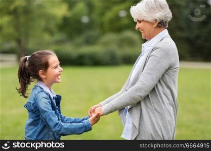 family, leisure and people concept - happy grandmother and granddaughter playing game or dancing at summer park. grandmother and granddaughter playing at park