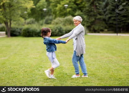 family, leisure and people concept - happy grandmother and granddaughter playing game or dancing at summer park. grandmother and granddaughter playing at park