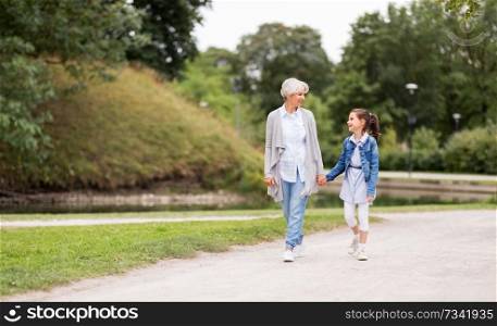 family, leisure and people concept - happy grandmother and granddaughter walking at summer park. grandmother and granddaughter walking at park