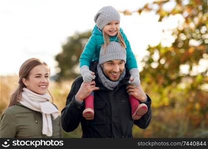 family, leisure and people concept - happy mother and father carrying little daughter on neck walking in autumn. happy family walking in autumn