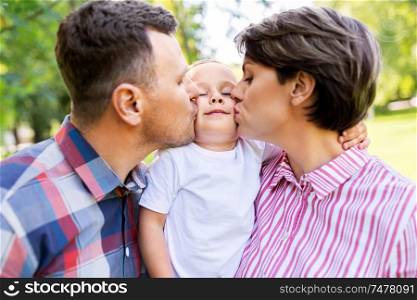 family, leisure and people concept - happy mother and father kissing their little son at summer park. mother and father kissing their little son at park