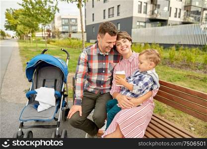 family, leisure and people concept - happy mother and father with little son in stroller and takeaway coffee sitting on street bench in city. family with baby in stroller and coffee in city