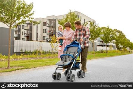 family, leisure and people concept - happy mother and father with little son and stroller walking along city street. family with baby and stroller walking along city