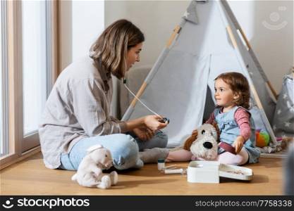 family, leisure and people concept - happy mother and little baby daughter playing doctor at home. mother and daughter playing doctor at home