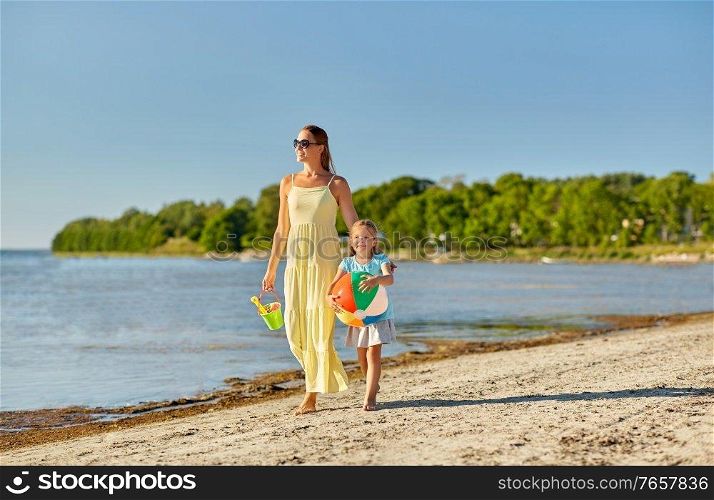 family, leisure and people concept - happy mother and little daughter with ball walking along summer beach. mother and daughter with ball walking along beach