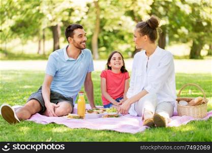 family, leisure and people concept - happy mother, father and daughter having picnic at summer park. happy family having picnic at summer park