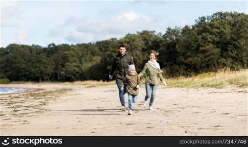 family, leisure and people concept - happy mother, father and little daughter running along autumn beach. happy family running along autumn beach