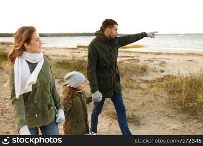 family, leisure and people concept - happy mother, father and little daughter walking along autumn beach. happy family walking along autumn beach