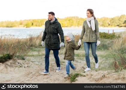 family, leisure and people concept - happy mother, father and little daughter walking along autumn beach. happy family walking along autumn beach