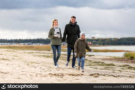 family, leisure and people concept - happy mother, father and little daughter walking along autumn beach. happy family walking along autumn beach