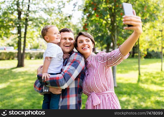 family, leisure and people concept - happy mother, father and little son taking selfie by smartphone at summer park. happy family taking selfie at summer park