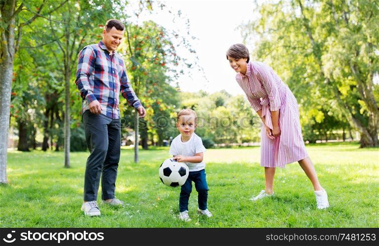 family, leisure and people concept - happy mother, father and little son with ball playing soccer at summer park. happy family playing soccer at summer park