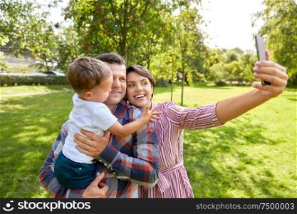 family, leisure and people concept - happy mother, father and little son taking selfie by smartphone at summer park. happy family taking selfie at summer park
