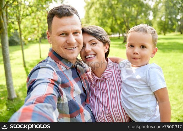 family, leisure and people concept - happy mother, father and little son taking selfie at summer park. happy family taking selfie at summer park