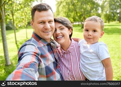 family, leisure and people concept - happy mother, father and little son taking selfie at summer park. happy family taking selfie at summer park