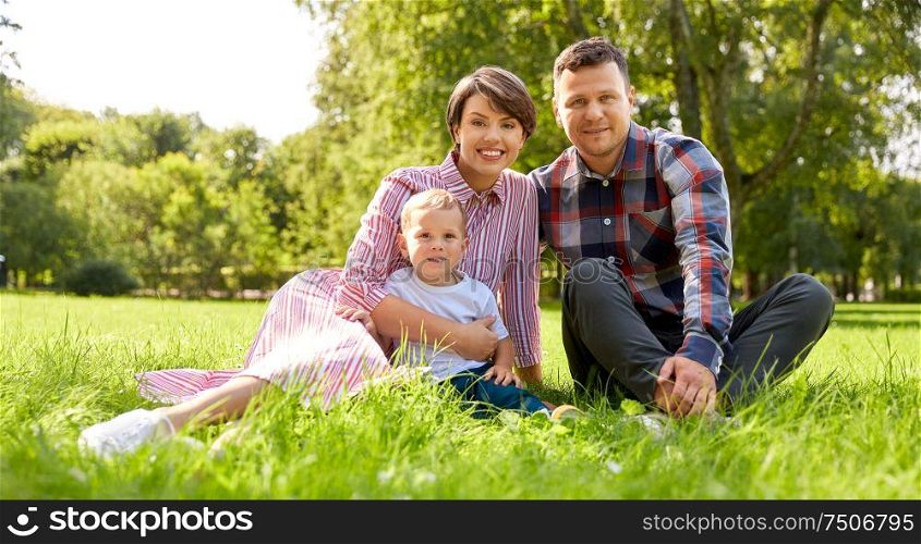 family, leisure and people concept - happy mother, father and little son at summer park sitting on grass. happy family at summer park sitting on grass