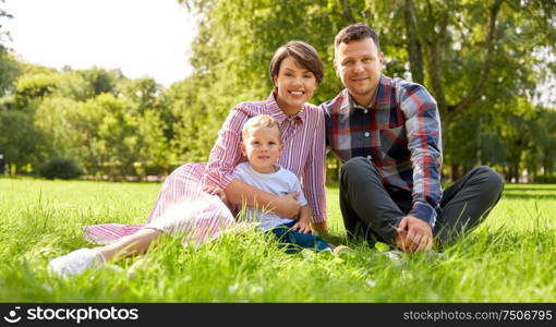 family, leisure and people concept - happy mother, father and little son at summer park sitting on grass. happy family at summer park sitting on grass