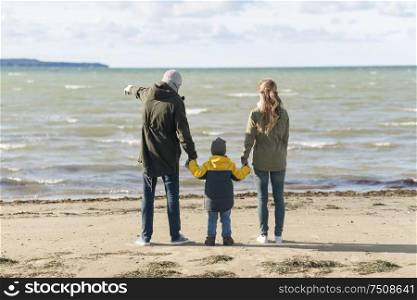 family, leisure and people concept - happy mother, father and little son at autumn beach looking at sea. happy family at autumn beach looking at sea