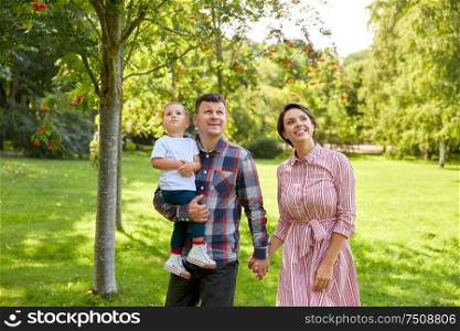 family, leisure and people concept - happy mother, father and little son looking up at summer park. happy family at summer park