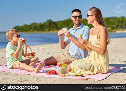 family, leisure and people concept - happy mother, father and little son having picnic on summer beach and eating sandwiches. happy family having picnic on summer beach