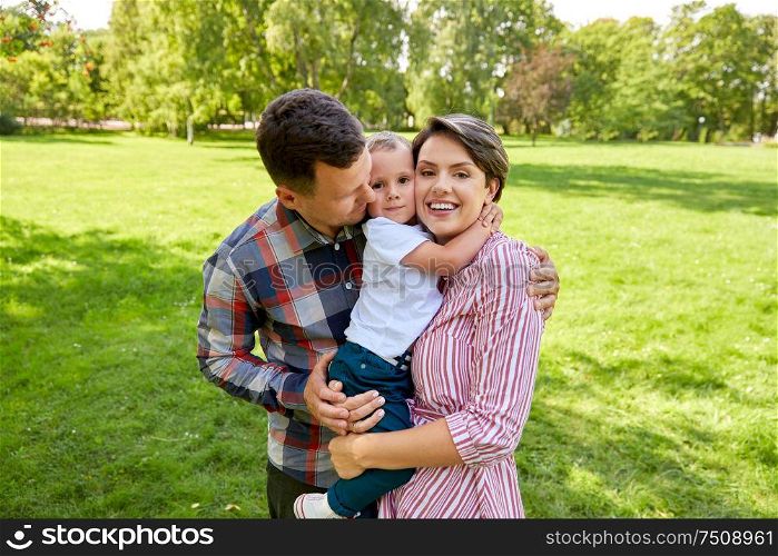 family, leisure and people concept - happy mother, father and little son hugging at summer park. happy family hugging at summer park
