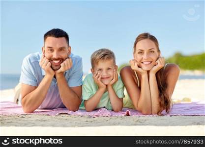 family, leisure and people concept - happy mother, father and little son lying on summer beach. happy family lying on summer beach