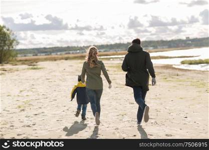 family, leisure and people concept - happy mother, father and little son running along autumn beach. happy family running along autumn beach