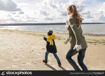 family, leisure and people concept - happy mother, father and little son running along autumn beach. happy family running along autumn beach