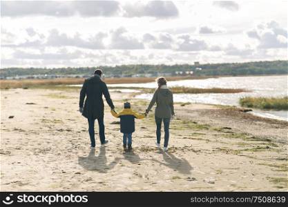family, leisure and people concept - happy mother, father and little son walking along autumn beach. happy family walking along autumn beach