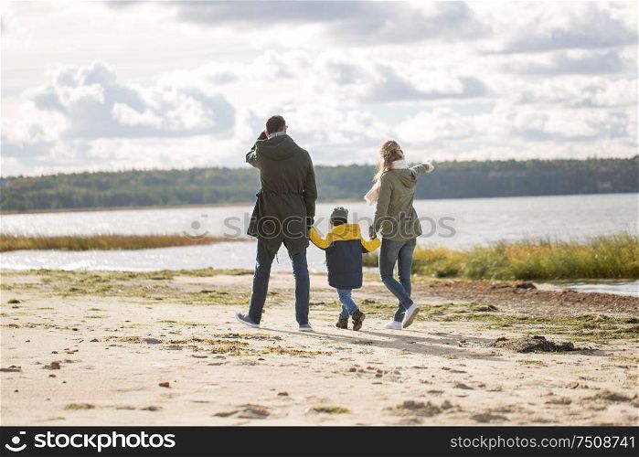 family, leisure and people concept - happy mother, father and little son walking along autumn beach. happy family walking along autumn beach