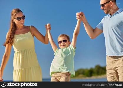 family, leisure and people concept - happy mother, father and little son walking along summer beach. happy family walking along summer beach