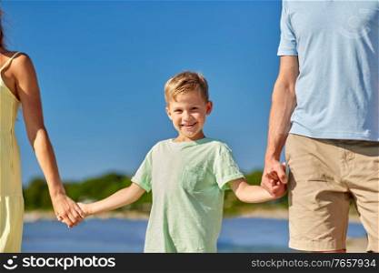 family, leisure and people concept - happy mother, father and little son walking along summer beach. happy family walking along summer beach