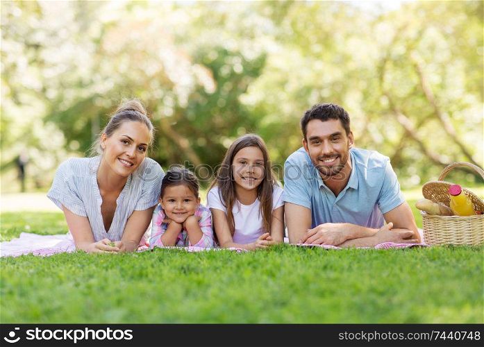 family, leisure and people concept - happy mother, father and two daughters laying on picnic blanket in summer park. family laying on picnic blanket in summer park