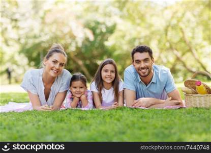 family, leisure and people concept - happy mother, father and two daughters laying on picnic blanket in summer park. family laying on picnic blanket in summer park
