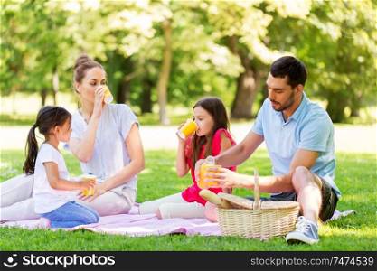 family, leisure and people concept - happy mother, father and two daughters having picnic and drinking orange juice at summer park. family drinking juice on picnic at summer park