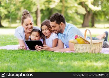 family, leisure and people concept - happy mother, father and two daughters with tablet computer laying on picnic blanket in summer park. family with tablet pc on picnic in summer park