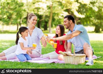 family, leisure and people concept - happy mother, father and two daughters having picnic and drinking orange juice at summer park. family drinking juice on picnic at summer park