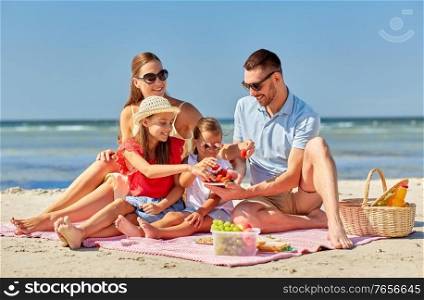 family, leisure and people concept - happy mother, father and two daughters having picnic on summer beach and eating strawberries. happy family having picnic on summer beach