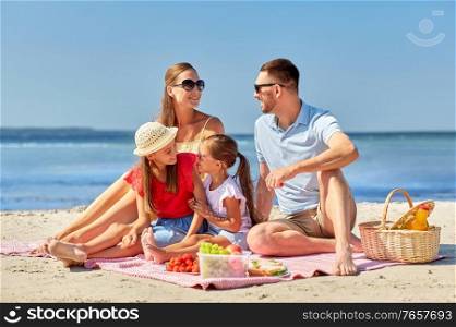 family, leisure and people concept - happy mother, father and two daughters having picnic on summer beach. happy family having picnic on summer beach