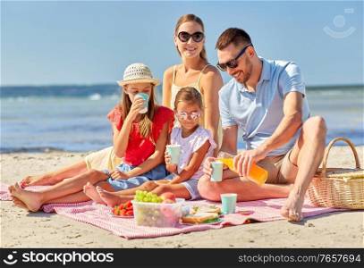 family, leisure and people concept - happy mother, father and two daughters having picnic on summer beach and drinking juice. happy family having picnic on summer beach